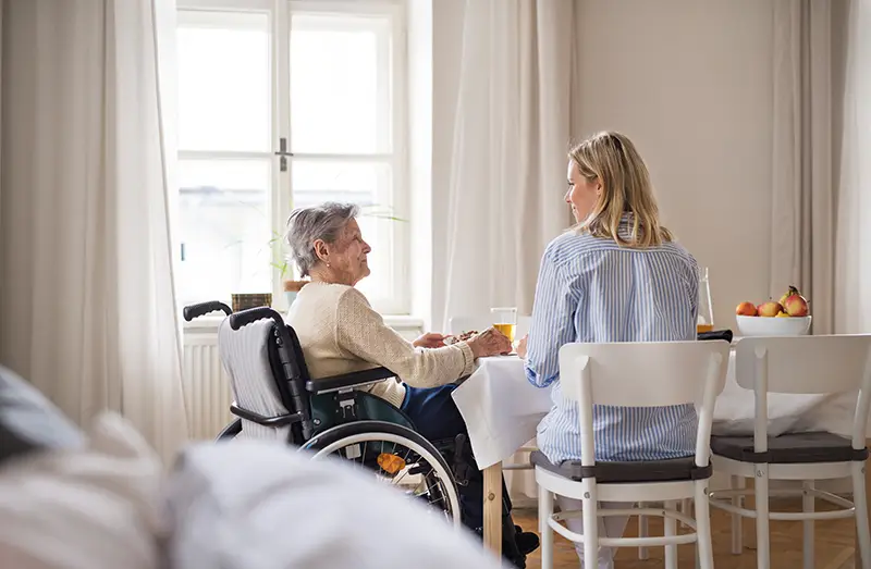 seniorin sitzt mit seniorenbetreuerin am wohnzimmertisch