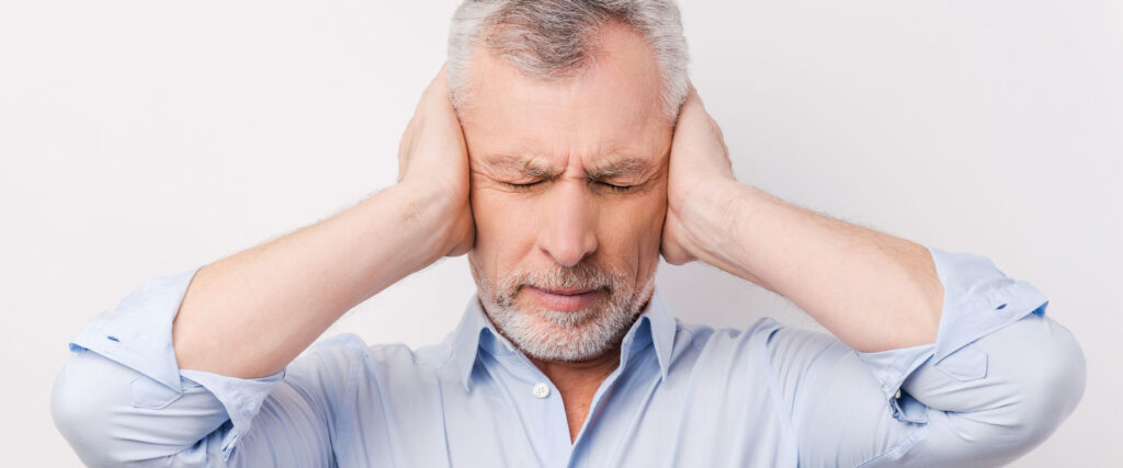 Tinnitus: Mann hält sich die Ohren zu, weil der Tinnitus zu laut ist