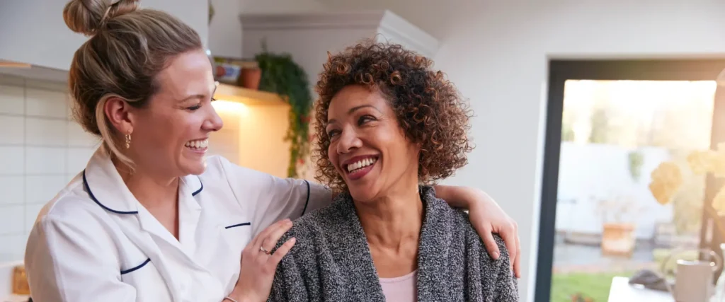 A caregiver hugs a smiling woman in a bright kitchen