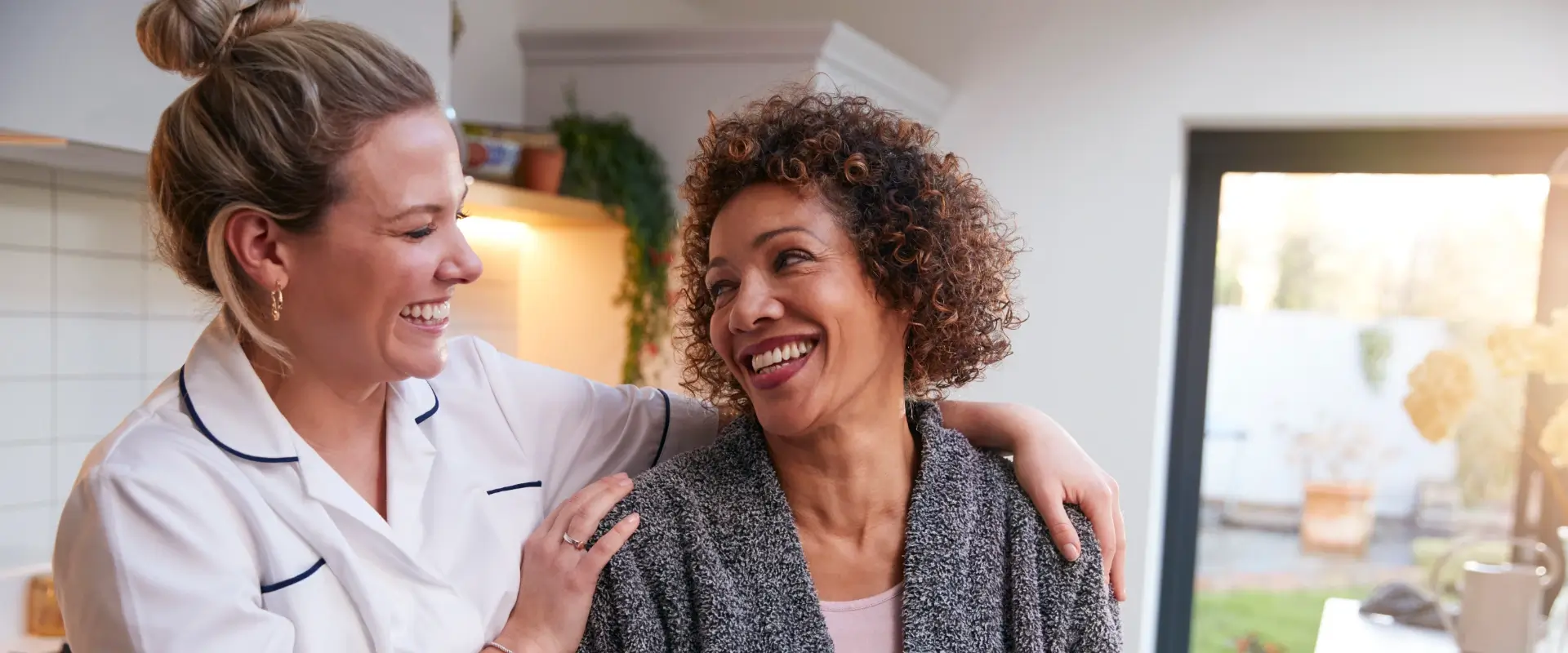 A caregiver hugs a smiling woman in a bright kitchen