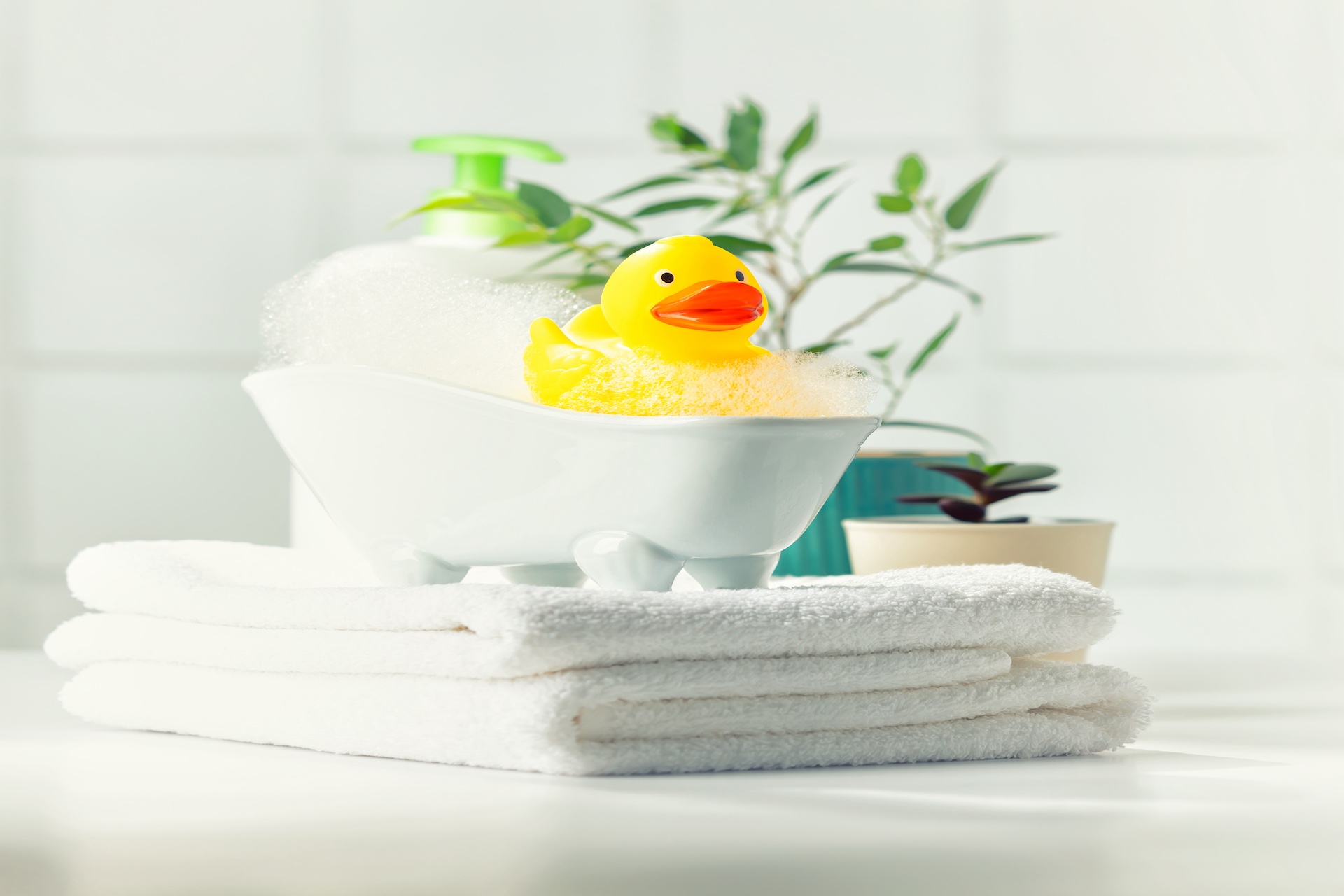 a miniature bubble bath, yellow rubber duck and white towels on bathroom countertop, children bath accessories, baby care