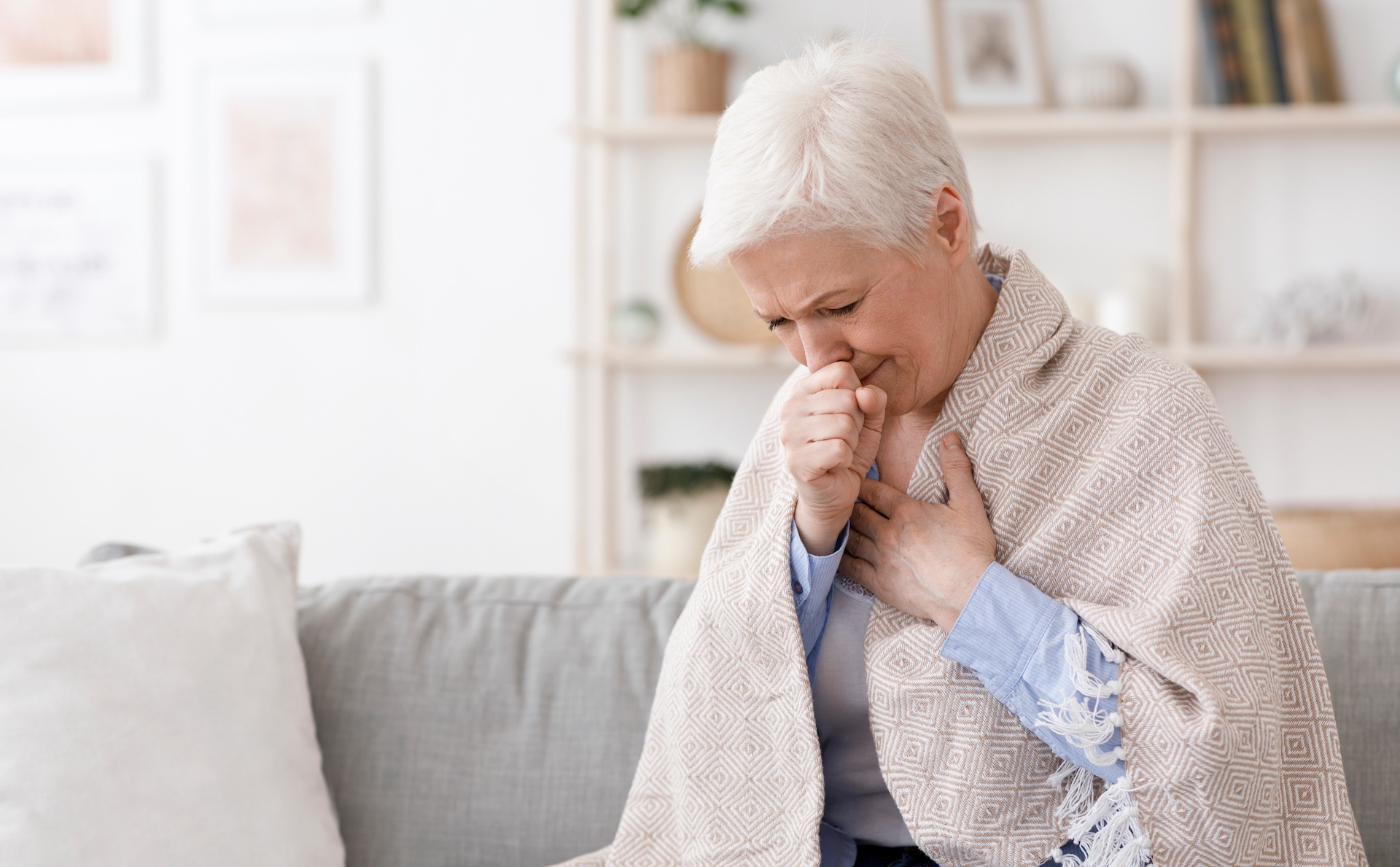 sick senior woman covered in blanket coughing hard at home