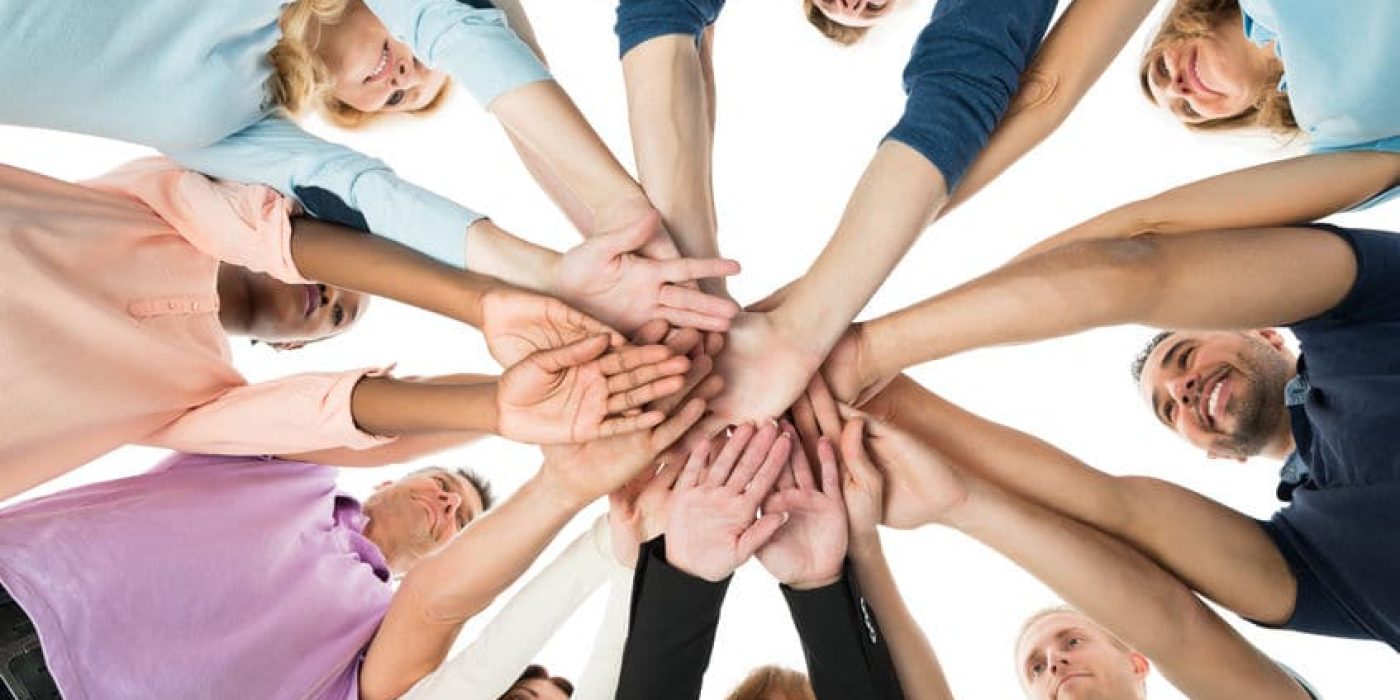 Directly below creative business team stacking hands while standing in huddle against white background