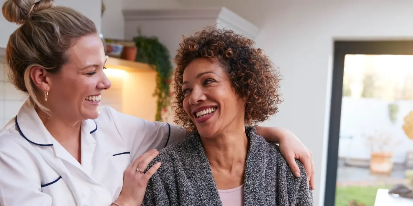 Pflegekraft umarmt lächelnde Frau in heller Küche