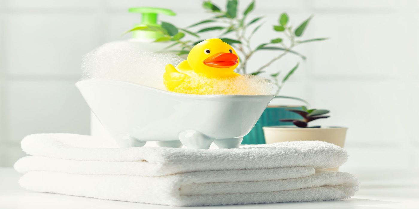 a miniature bubble bath, yellow rubber duck and white towels on bathroom countertop, children bath accessories, baby care