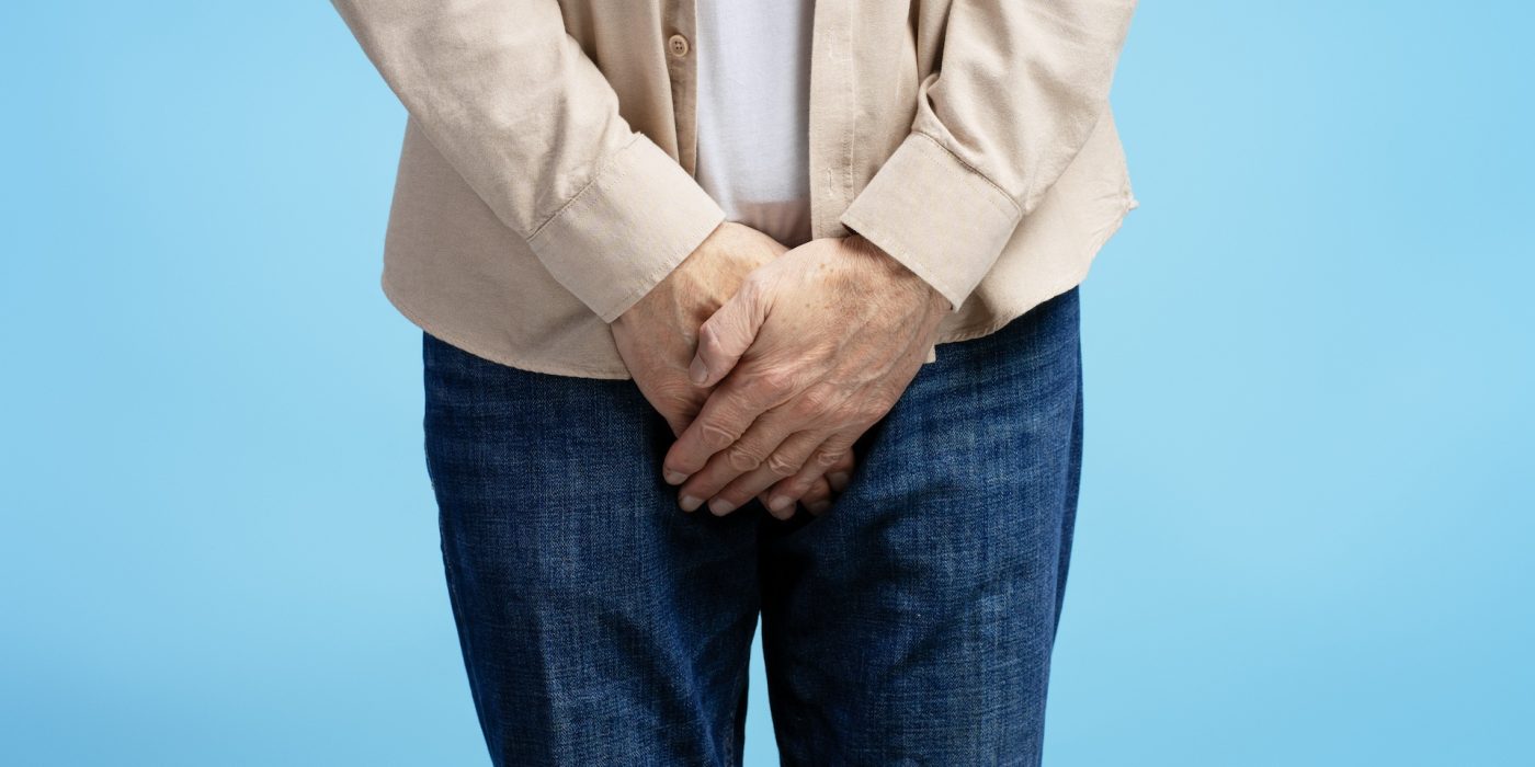 senior man experiencing discomfort holding groin area on blue background
