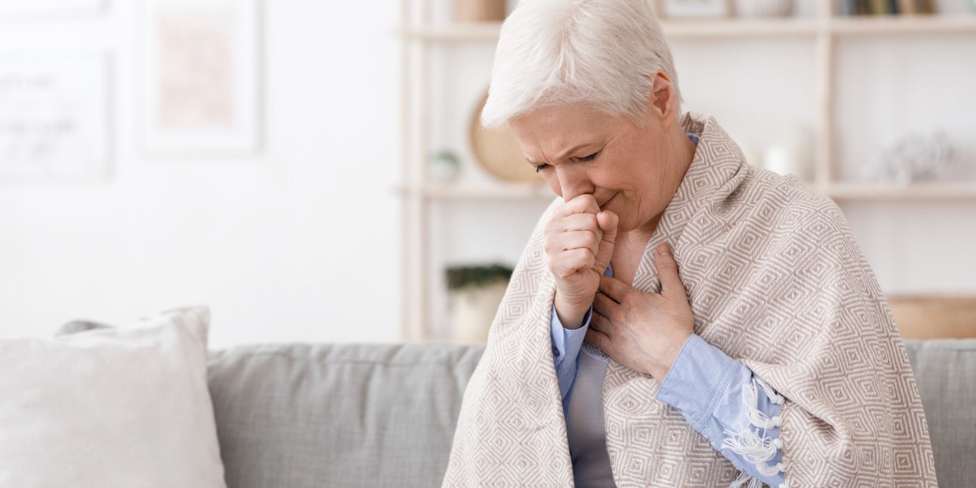 sick senior woman covered in blanket coughing hard at home