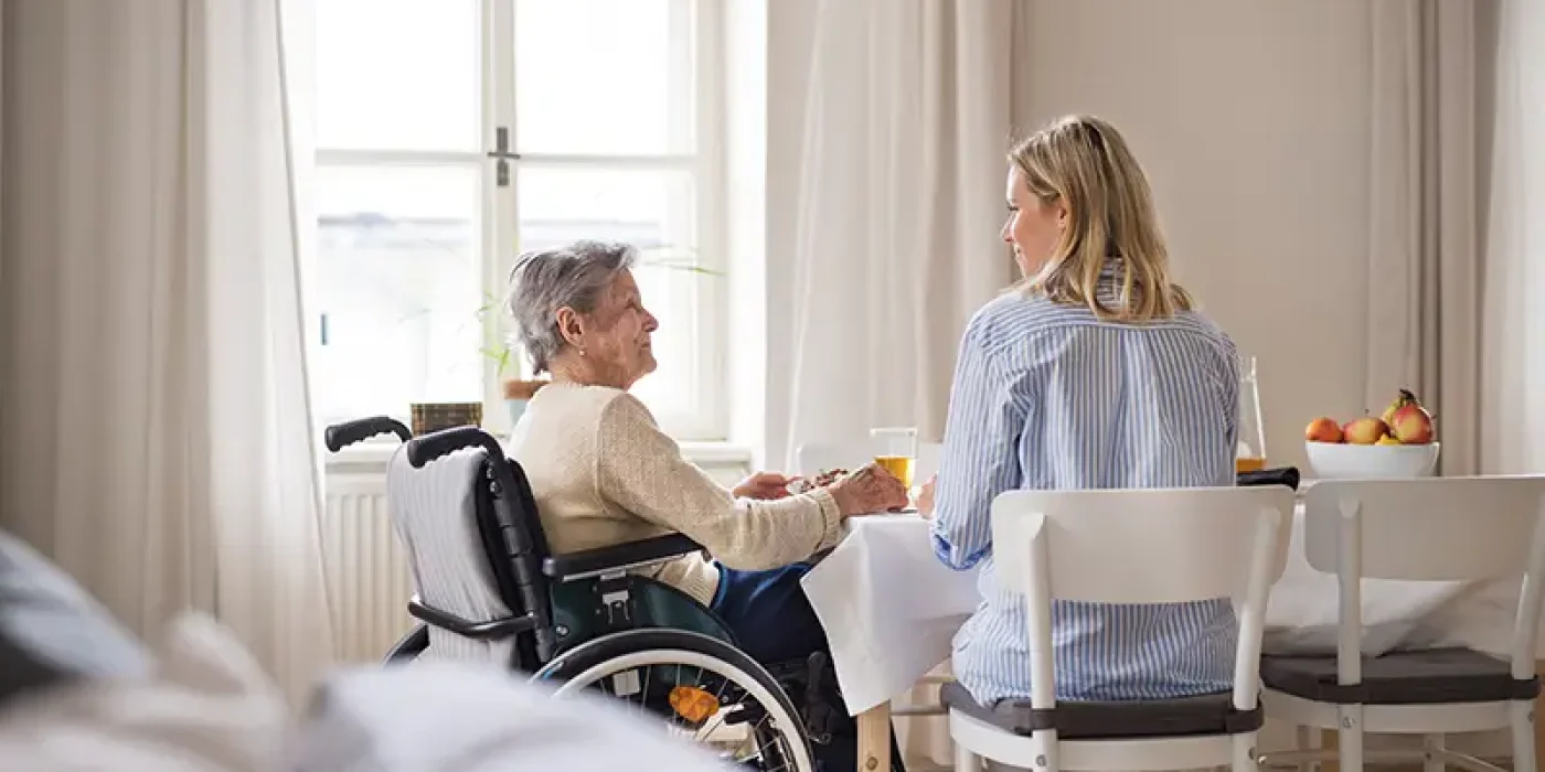 seniorin sitzt mit seniorenbetreuerin am wohnzimmertisch